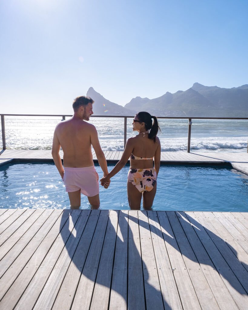 couple man and woman in front of Infinity pool looking out over the ocean of Cape Town South Africa, man and woman in swimming pool during sunset couple man and women in front of Infinity pool looking out over the ocean of Cape Town South Africa, man and woman in swimming pool during sunset.
